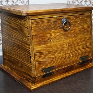 Puede incluir: Una panera de madera con puerta con bisagras y un tirador de anillo met&aacute;lico. La caja est&aacute; hecha de madera te&ntilde;ida con vetas visibles y bisagras met&aacute;licas. El dise&ntilde;o es r&uacute;stico y adecuado para el almacenamiento en la cocina.