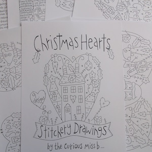 Op de afbeelding: Zwart-witte lijntekening van een kerst hart met een huis, bomen en sterren. De tekst "Christmas Hearts" en "Stitchery Drawings by the Curious Miss b..." is in de afbeelding opgenomen.