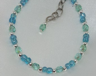Puede incluir: Una delicada pulsera con cuentas azules y verdes alternas con detalles plateados. La pulsera tiene un cierre de acero inoxidable y una pequeña cuenta colgante. Las cuentas son una mezcla de formas redondas y facetadas.