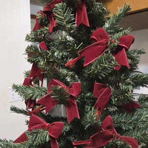 May include: A small artificial Christmas tree adorned with many deep red velvet bows. The bows are evenly spaced across the green branches, creating a festive holiday display.