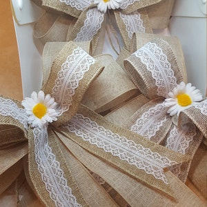 Peut inclure: Trois nœuds en toile de jute avec une bordure en dentelle blanche et des embellissements de marguerites jaunes. Les nœuds sont liés ensemble avec de la ficelle.