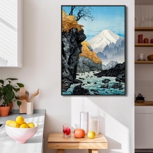 May include: A Japanese woodblock print depicting a mountain scene with a river flowing through a rocky gorge. The mountain is snow-capped and the river is filled with white rapids. The print is framed in black.