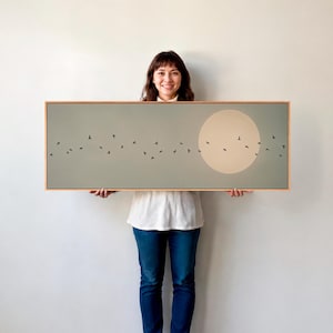 May include: A rectangular landscape painting in a light wood frame featuring a muted sage green background with a large, pale circular moon on the right side and a flock of small black birds flying in a scattered horizontal line across the centre.