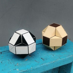 Peut inclure: Deux puzzles géométriques, l'un noir et blanc et l'autre brun et crème, sont posés sur un tabouret en bois bleu. Le tabouret est sur un sol en bois blanc.