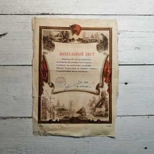 May include: A vintage, yellowed, paper certificate with red and gold accents. The certificate reads "POXBAЛЬНЫЙ ЛИСТ" and is signed with a handwritten signature. The certificate features a red star and a depiction of a train.