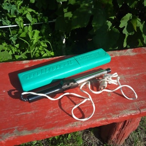 Peut inclure: Un fer à souder électrique vert et noir avec un cordon blanc et un étui en plastique vert. L'étui porte l'inscription "SOLDERING IRON".