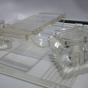May include: A clear glass desk organiser with three compartments. The organiser has a raised, textured surface and a clear lid.