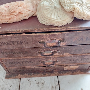 May include: A wooden box with four drawers labeled "Busettes", "Repriser", "Repriser", and "Ala 2". The box is decorated with three white lace doilies.