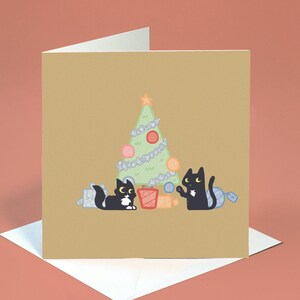 May include: A Christmas card featuring two black cats decorating a green Christmas tree with baubles and presents. The card has a brown background.