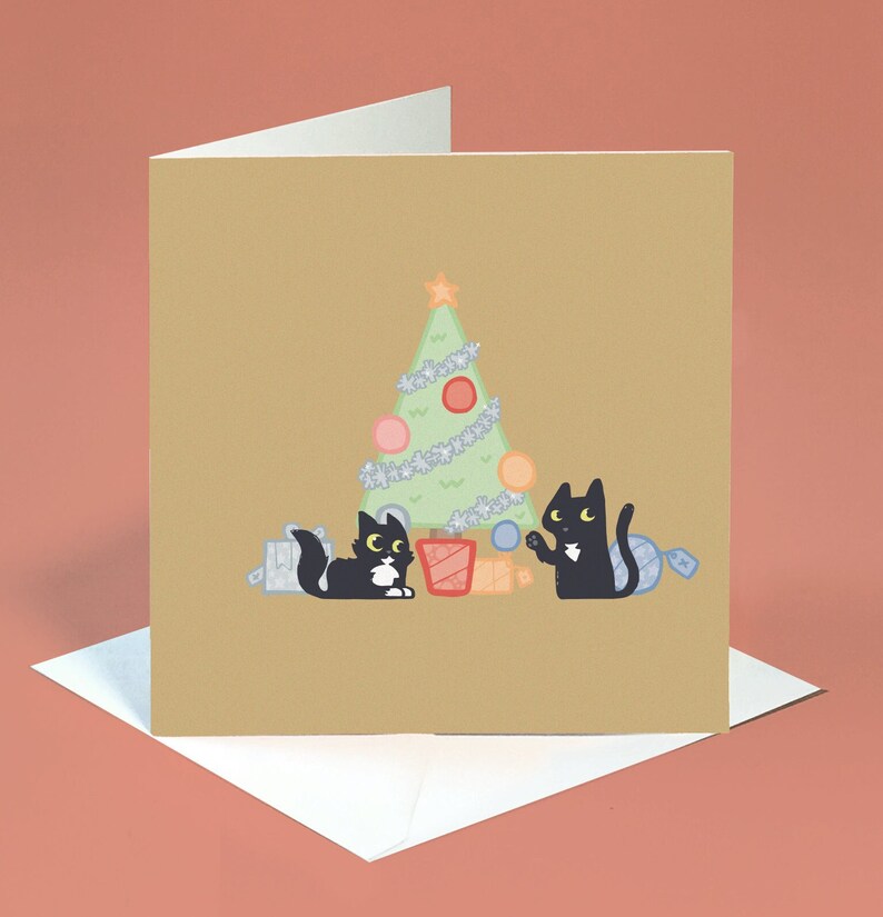 May include: A Christmas card featuring two black cats decorating a green Christmas tree with baubles and presents. The card has a brown background.