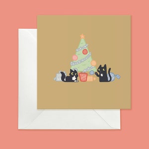 May include: A Christmas card featuring two black cats with yellow eyes, one holding a red bauble and the other holding a blue bauble, standing in front of a green Christmas tree with white lights and red and pink baubles. The card has a brown background.