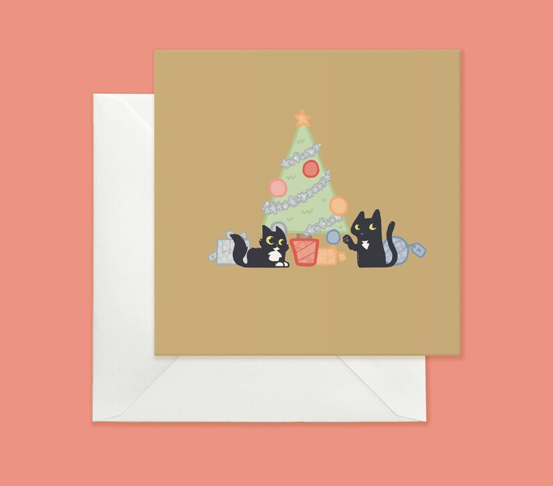 May include: A Christmas card featuring two black cats with yellow eyes, one holding a red bauble and the other holding a blue bauble, standing in front of a green Christmas tree with white lights and red and pink baubles. The card has a brown background.