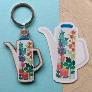 May include: A wooden keychain shaped like a watering can with a floral design. The watering can is painted white with blue, red, orange, yellow, and purple flowers. The keychain has a silver key ring.