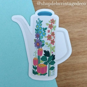 May include: White ceramic pitcher with a blue handle and a floral design. The flowers are pink, yellow, blue, and green. The pitcher is a vintage style.