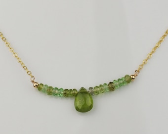 May include: A gold chain necklace with a teardrop-shaped green gemstone pendant and a row of smaller green gemstones.