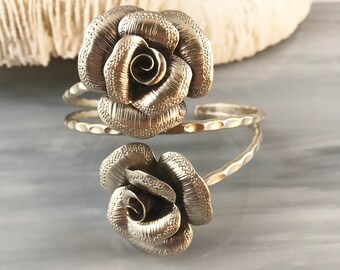 May include: A silver bracelet with two rose-shaped charms. The bracelet is made of hammered metal and has a textured finish.