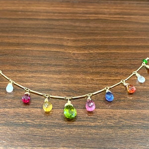 May include: A gold chain necklace with a variety of colored gemstone drops. The gemstones include blue, green, red, yellow, and orange.