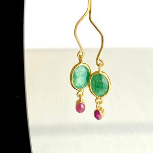 May include: Gold earrings with green and pink gemstones. The earrings feature a dangling design with a larger green gemstone and a smaller pink gemstone.