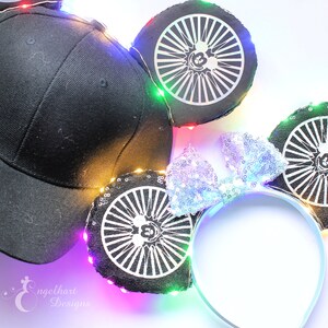 Può includere: Cappellino da baseball nero e un paio di orecchie da topo con un fiocco argentato. Le orecchie sono nere con un design a ruota bianca e una silhouette di Topolino. Le orecchie e il cappellino sono decorate con luci a LED colorate.