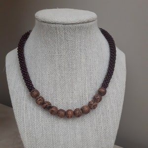 May include: A brown beaded necklace with a row of larger brown wood beads in the centre.