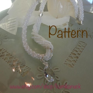 May include: A white beaded necklace with a crystal pendant, displayed on a pair of white ceramic doves. The necklace is made of multiple strands of beads and has a delicate, feminine look. The doves are kissing, symbolising love and peace. The text "Pattern" is visible in the image.