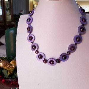 May include: A purple necklace featuring round iridescent beads. The beads have a darker purple centre and a lighter purple outer ring.
