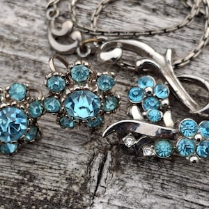 May include: A silver necklace with a floral design and blue rhinestone accents. The necklace is paired with a set of matching earrings with blue rhinestones.