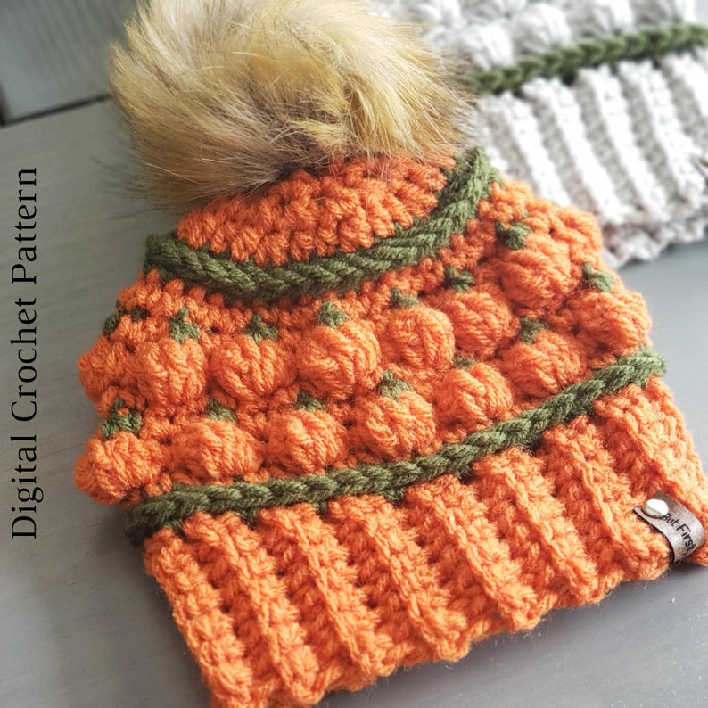May include: Orange and green crocheted beanie with a faux fur pom pom. The beanie has a textured pumpkin design and a brown leather tag that says "Knit First".