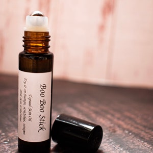 Puede incluir: Un frasco de vidrio marrón con una tapa negra y una etiqueta blanca que dice "Boo Boo Stick Topical Skin Oil Try it on bumps, scratches, scrapes and skin irritations."
