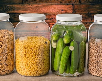 May include: Four clear glass jars with white lids filled with different pantry staples. The jars are lined up on a wooden surface. The jars contain pasta, pickles, cereal, and beans.