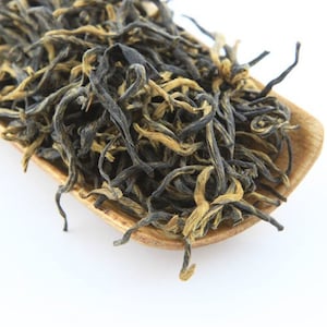 May include: A close-up of loose leaf black tea with golden tips. The tea is in a wooden bowl.