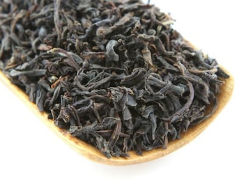 May include: Loose black tea leaves in a wooden spoon. The tea leaves are dark brown and have a slightly curled shape.