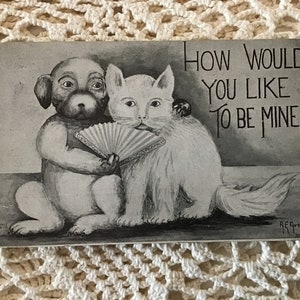 May include: Black and white vintage postcard featuring a dog and cat with a hand fan. The text on the postcard reads "How would you like to be mine?"