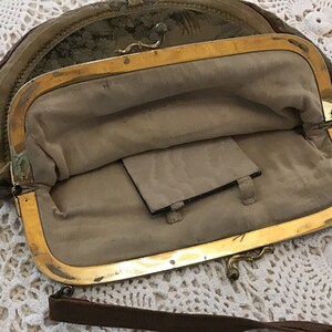 K&ouml;nnte beinhalten: Eine vintage, halbmondf&ouml;rmige Handtasche mit einem goldenen Verschluss und einem braunen Lederriemen. Die Tasche ist mit einem beigefarbenen Stoff gef&uuml;ttert und hat eine kleine Tasche im Inneren.