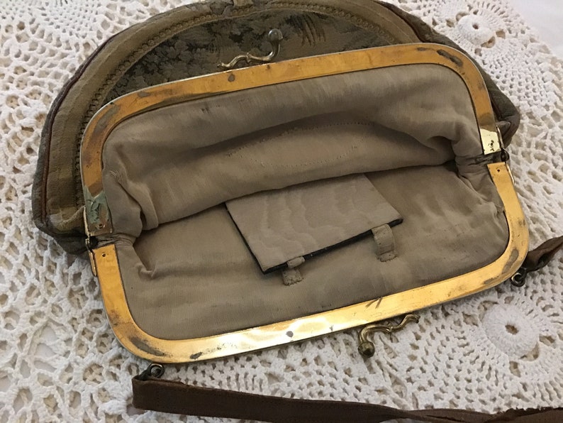 K&ouml;nnte beinhalten: Eine vintage, halbmondf&ouml;rmige Handtasche mit einem goldenen Verschluss und einem braunen Lederriemen. Die Tasche ist mit einem beigefarbenen Stoff gef&uuml;ttert und hat eine kleine Tasche im Inneren.
