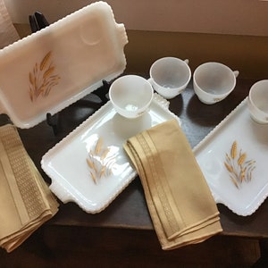 Puede incluir: Juego de cuatro bandejas de servir de vidrio de leche blanco con diseño de trigo dorado. Cada bandeja tiene una pequeña hendidura para una taza. El juego también incluye cuatro tazas de vidrio de leche blanco y cuatro servilletas beige con ribetes dorados.