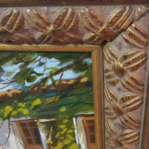 Puede incluir: Una pintura al &oacute;leo enmarcada que representa una caba&ntilde;a con un exterior blanco y puertas de madera marr&oacute;n. La caba&ntilde;a est&aacute; rodeada de exuberante vegetaci&oacute;n verde y &aacute;rboles. El marco es de color dorado con un dise&ntilde;o decorativo.