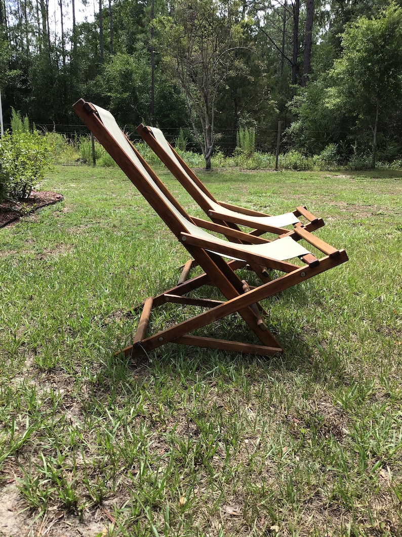 May include: Two wooden folding chairs with white canvas seats are sitting on a grassy lawn. The chairs are in a relaxed position, with the backs leaning back.