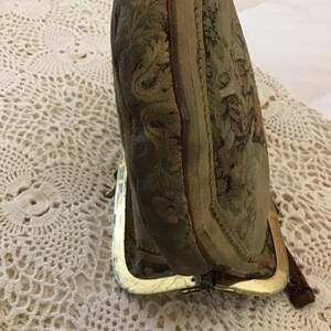 K&ouml;nnte beinhalten: Eine vintage Geldb&ouml;rse aus Tapisserie-Stoff mit einem goldenen Metallrahmen und einem floralen Design. Die B&ouml;rse ist geschlossen und der Rahmen ist sichtbar.