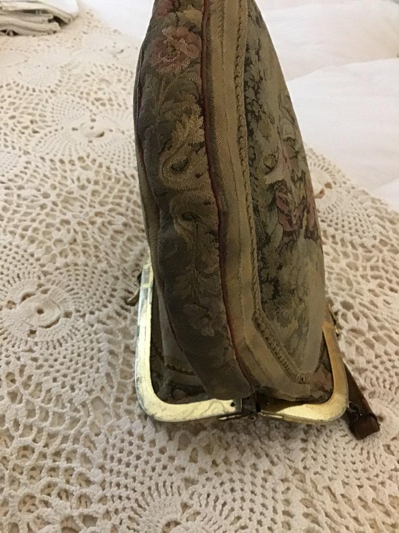 K&ouml;nnte beinhalten: Eine vintage Geldb&ouml;rse aus Tapisserie-Stoff mit einem goldenen Metallrahmen und einem floralen Design. Die B&ouml;rse ist geschlossen und der Rahmen ist sichtbar.