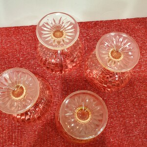 May include: Four pink glass dessert dishes with a textured pattern. The dishes are upside down, showing the bottom of the dishes.