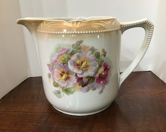 May include: A white porcelain pitcher with a gold rim and floral design. The flowers are pink, purple, and yellow pansies.