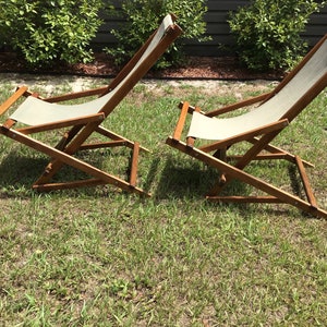 May include: Two wooden folding chairs with canvas seats. The chairs are in a reclined position and are on a grassy lawn.