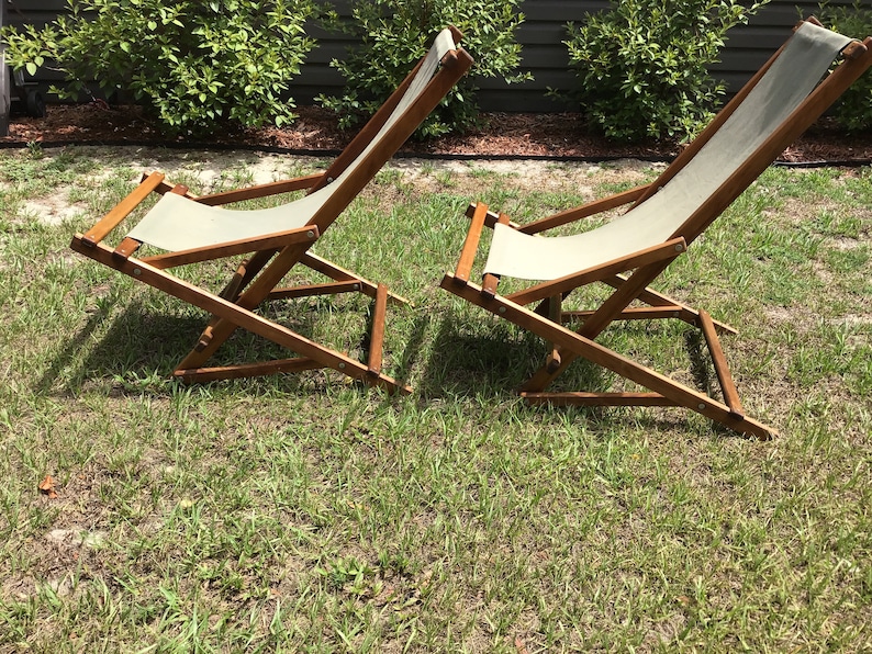 May include: Two wooden folding chairs with canvas seats. The chairs are in a reclined position and are on a grassy lawn.