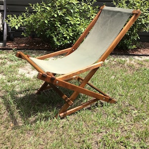 May include: A wooden folding chair with a canvas seat and back. The chair is in a grassy area.