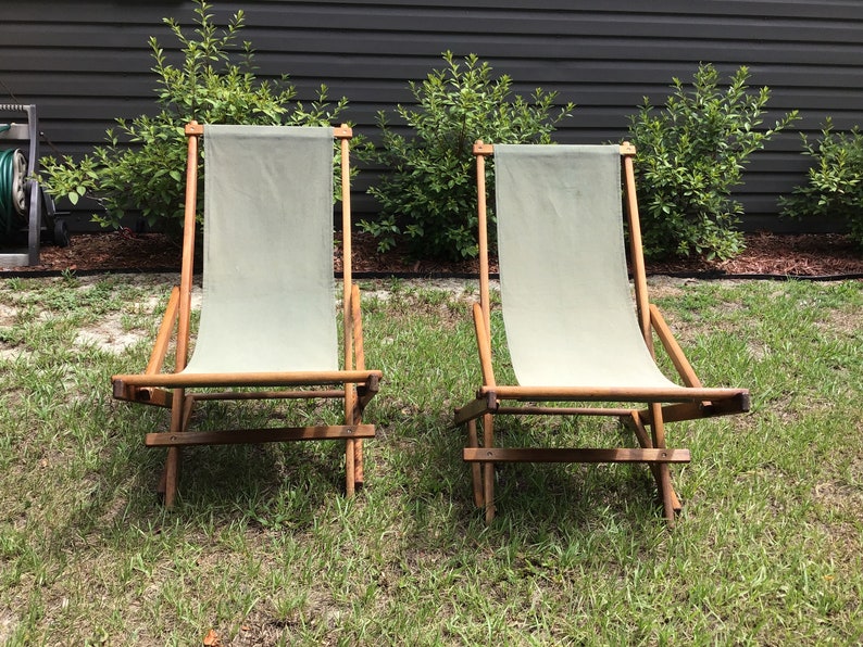 May include: Two wooden folding chairs with canvas seats. The chairs are in a grassy area and are facing each other.