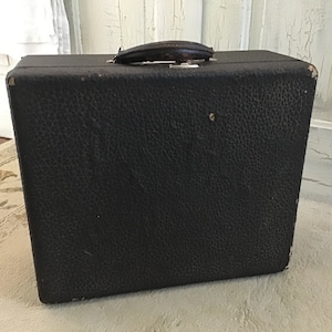 Puede incluir: Una maleta vintage negra con textura de cuero y un asa marrón.