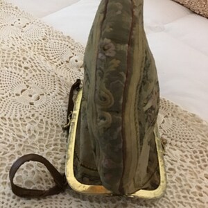 K&ouml;nnte beinhalten: Eine vintage Geldb&ouml;rse aus Tapisserie-Stoff mit einem goldenen Metallrahmen und einem braunen Lederriemen.