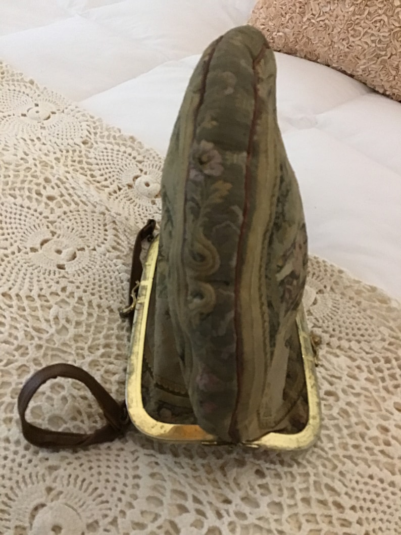 K&ouml;nnte beinhalten: Eine vintage Geldb&ouml;rse aus Tapisserie-Stoff mit einem goldenen Metallrahmen und einem braunen Lederriemen.
