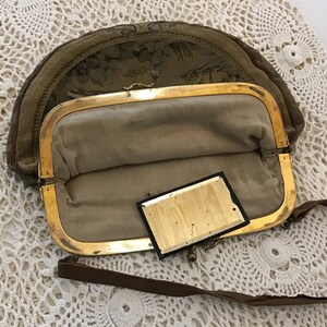 K&ouml;nnte beinhalten: Eine vintage, halbmondf&ouml;rmige Handtasche mit einem goldenen Verschluss und einem braunen Riemen. Die Tasche ist aus einem Stoff mit Blumenmuster und hat einen kleinen, rechteckigen Spiegel im Inneren.
